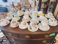 Multiple rows of floral bone-china tea cup and saucer sets displayed on dresser