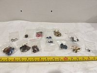 Overview of ten plastic bags with assorted jewelry items next to measuring tape