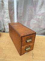 Front angled view showing oak cabinet, two drawers with brass pulls and label slots