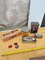 Group shot of all eight vintage tins with measuring tape for scale