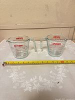 Two Pyrex 2-cup measuring cups side by side with measuring tape for scale