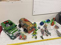 Wide view of entire lot showing two large vehicles, two motorcycles, multiple bagged action figures, measuring tape for scale