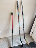 Three hockey sticks leaning against wall showing full length