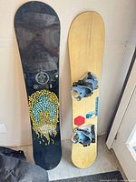 Two Burton snowboards upright with bindings on one and travel bag on floor