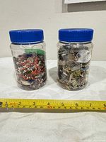 Two jars of assorted broken jewelry pieces shown side by side with measuring tape for scale