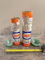 Front view of both Tinkertoy tubes with measuring tape for scale and separate green lids