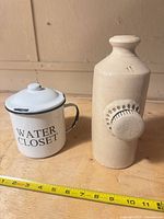 Enamel mug and stoneware hot water bottle upright with ruler for scale
