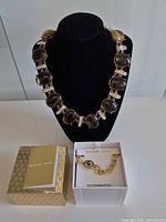Both necklaces displayed; Michael Kors boxed, Banana Republic collar on stand