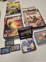 Overview showing GBA SP open with cartridges, PC game cases, sealed card set