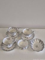 Front view of three teacups each on saucer, sugar bowl and pin dish, showing pattern and script