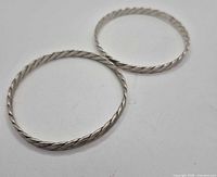 Two twisted rope silver-tone bangles on white background