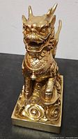 Front view of gold tone winged dragon foo dog statue on square base