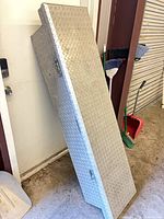 Full view of closed diamond-plate toolbox leaning against wall