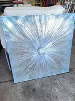 Front view of silver starburst canvas art leaning against furniture
