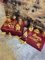 Group shot of all 16 gold ornaments displayed on two burgundy Danbury Mint boxes