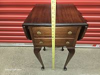 Front view of mahogany drop-leaf table showing two drawers, cabriole legs, measuring tape for height