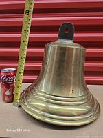Side view of brass ship’s bell beside soda can and measuring tape showing approx 12 in height