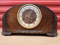 Front view of wooden cathedral-top mantel clock showing dial, bezel and carved applique