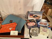 Overall lot showing boxed cheese board, microwave cookware, placemats, cutters, rack