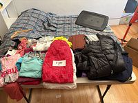 Overall view of folded women’s clothing on table: jacket, tops, red garment, hanger visible