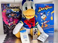 Donald Duck plush centered with two comics behind and metal tag in front