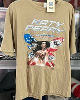 Front view of beige T-shirt with Katy Perry superhero graphic and tour name