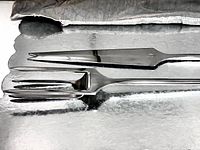 Close-up of carving knife and fork stacked to show blade, serration, fork tines and polished finish