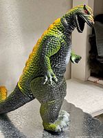 Front and side view of articulated Dormell Godzilla figure showing yellow dorsal stripe and stance