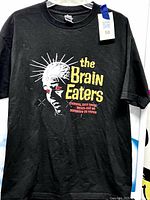 Front view of black "The Brain Eaters" graphic T-shirt hanging on hanger