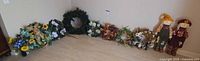 Row of seven wreaths and two standing scarecrow dolls displayed against wall