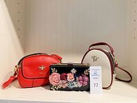 Three handbags grouped: red crossbody, black floral clutch, white rounded crossbody