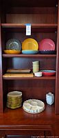 Cabinet view showing stacked plates, patterned bowls, ramekins, egg platter and boards