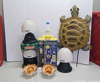 Front view of all items including Coleman lamp, boxed oil lamp, two lotus lights, turtle stake