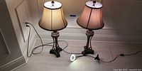 Two matching bronze table lamps with bell shades side by side plugged in, clip-on light on floor