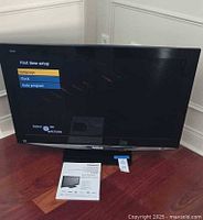 Front view of powered-on Panasonic 37" TV showing setup screen with manual and stand visible