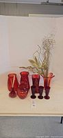 Group shot of all red glass vases, goblets and faux stems on table