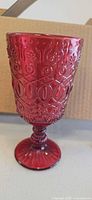 Single ruby red pressed glass goblet close-up showing embossed pattern and stem