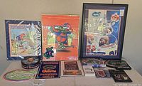 Overview of entire lot on table with three framed posters, signs, tins, books and game