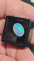 Front view of oval Ethiopian opal in display box showing vivid green and blue flashes