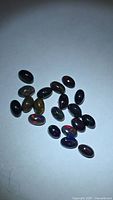 Group of 19 oval black opal cabochons showing play-of-color