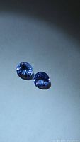 Two round violet-blue faceted stones on neutral background