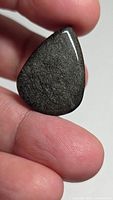 Front view of polished pear silver sheen obsidian cabochon held between fingers
