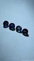 Four round teal blue sapphires on white surface, side lighting shows body colour