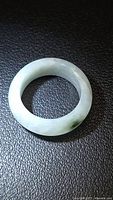 Top view of polished jade ring showing light green/off-white color and dark green inclusion