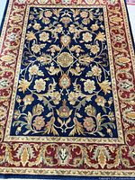 Full view of rug showing navy field, red border, floral motifs and fringe