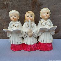 Front view of ceramic choir planter showing three singers, red base, white robes, gold accents