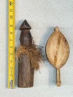 African wood figure and leaf-shaped paddle beside tape for scale