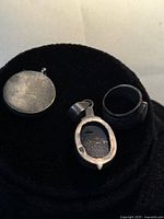 Backs of pendant, brooch and interior of ring displayed on black stand