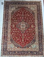 Full view of Persian Kashan carpet showing red field, central medallion and navy borders