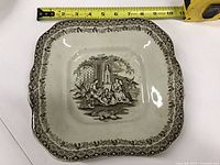 Full view of square brown transferware dish with measuring tape showing approx 9.5 in width